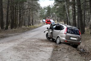 droga przez las, po prawej stronie na poboczu rozbity samochód osobowy, w tle służby ratunkowe