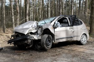 rozbity samochód osobowy stojący na poboczu drogi, w tle las