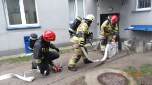 Strażacy rozwijają specjalistyczny sprzęt przed budynkiem komendy