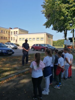 Policjant rozmawia z dziećmi na placu przed szkołą o bezpieczeństwie na drodze