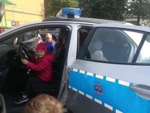 Przedszkolaki zwiedzają radiowóz, dziewczynka siedzi na miejscu kierowcy