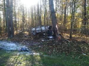 Zdjęcie z miejsca wypadku, samochód koloru srebrnego przechylony na jedną stronę pomiędzy drzewami