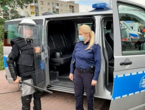 umundurowana policjantka stojąca przy radiowozie pozuje do zdjęcia z dzieckiem ubranym w sprzęt przeciwuderzeniowy