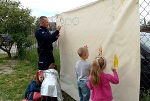 umundurowany policjant rysuje z przedszkolakami w ramach spotkania z okazji Dania Dziecka