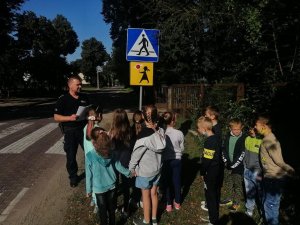 umundurowany policjant stojący przy oznakowanym przejściu dla pieszych wraz z grupą dzieci