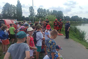 umundurowana policjantka i strażacy stojący przed grupą dzieci w pobliżu akwenu Rutki