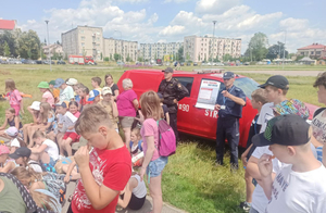 umundurowany policjant i strażak stojący przy samochodzie strażackim przed grupą dzieci