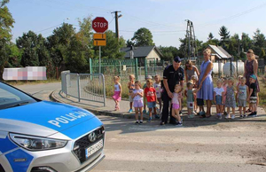Umundurowany policjant stojący z grupą dzieci przy przejściu dla pieszych
