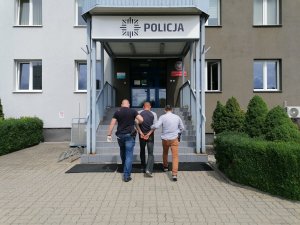 dwóch policjantów doprowadza podejrzanego do budynku komendy policji