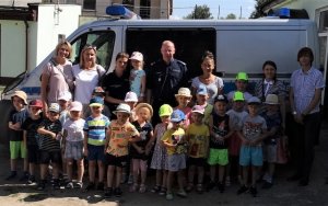 Dzieci wraz z opiekunami i funkcjonariuszami Policji podczas wizyty w pułtuskiej komendzie na tle radiowozu