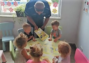 Policjant wręcza dzieciom kolorowanki, udziela wskazówek podczas korzystania z numerów ratunkowych
