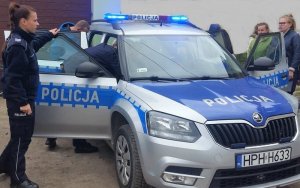 Radiowóz policyjny z włączonymi sygnałami błyskowymi i uczniowie podczas spotkania z policjantami