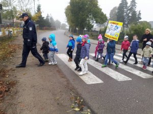Policjant przeprowadza dzieci po przejściu dla pieszych.