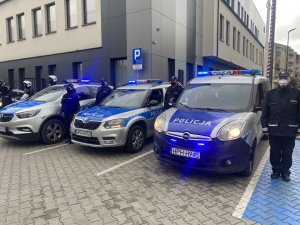 Policjanci stojący przy Komendzie Powiatowej Policji w Sochaczewie na baczność obok radiowozów i motocykli z włączonymi sygnałami dźwiękowymi i świetlnymi