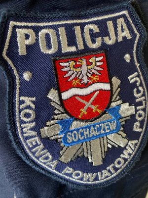 Emblemat na mundurze z logo policji w kształcie gwiazdy na którym nałożono herb powiatu sochaczewskiego. Na górze napis Policja, a od górnej lewej krawędzi w dół, aż do prawej górnej krawędzi jest napis Komenda Powiatowa Policji