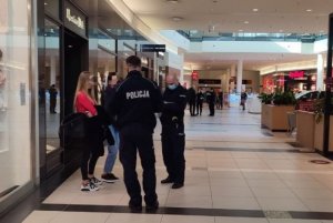 Dwóch umundurowanych policjantów stoi przy dwóch kobietach w galerii handlowej
