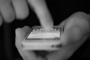Smartfon trzymany w dłoni z wyświetlaną klawiaturą dotykową. Na zdjęciu widać palec dotykający ekranu