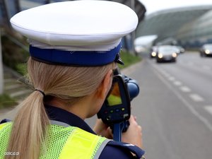 Policjantka patrzy w urządzenie do pomiaru prędkości nakierowane na nadjeżdżające pojazdy