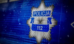 Logo policji w postaci srebrnej ośmioramiennej gwiazdy. W górnej jej części na niebieskim pasku napis Policja, na środku na niebieskim pasku jest napis 112
