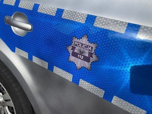 Na zdjęciu widać tylne drzwi radiowozu na których umieszczono logo policji w kształcie ośmioramiennej gwiazdy. W środku umieszczono napis 112