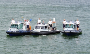 Trzy łodzie policyjne na wodzie. Na łodziach stoją policjanci