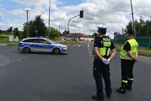 Policjant i druh OSP obserwują radiowóz wjeżdżający na skrzyżowanie