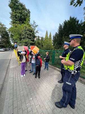 Policjanci ruchu drogowego stoją na chodniku a obok nich dzieci