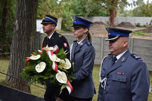 Strażak, policjantka z wiązanką z biało-czerwonych kwiatów i policjant