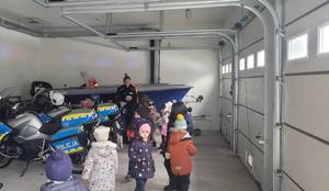 Policjantka z dziećmi stoją w garażu. Na zdjęciu widać dwa motocykle i policyjną łódź
