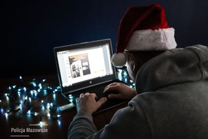 Siedzący tyłem mężczyzna w szarej bluzie i czapką świętego Mikołaja patrzy w monitor laptopa. Z lewej strony na dole napis Policja Mazowsze