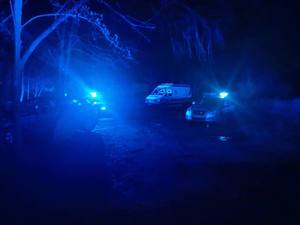 Zdjęcie zrobione nocą. Na zdjęciu widać włączone sygnały świetlne koloru niebieskiego nadawane z policyjnych radiowozów. W tle karetka pogotowia.