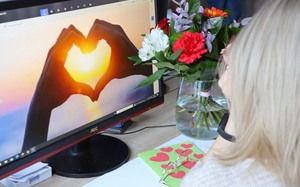 Kobieta patrzące w monitor na którym witać ręce złożone w serce