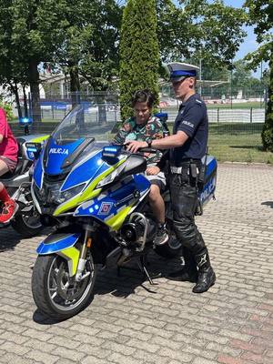 Dziecko siedzi na motocyklu. Obok stoi policjant