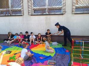 Policjantka rozdaje ulotki dzieciom siedzącym na ziemi