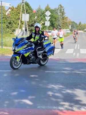 Policjant na motocyklu, a za nim widać biegnące osoby