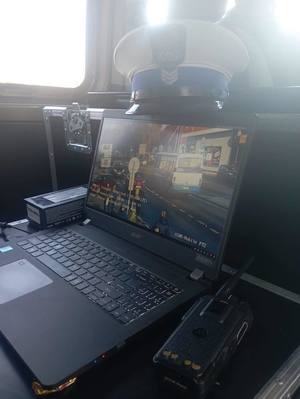 Zdjęcia przedstawia część pasażerską wnętrza busa. Na laptopie jest podgląd na ulicę. Nad laptopem leży czapka czapka służbowa policjanta