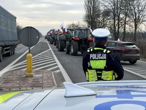 Policjant patrzy w kierunku ciągników rolniczych wjeżdżających na drogę