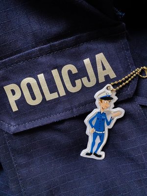 Fragmenty munduru ćwiczebnego z napisem Policja. Na nim leży odblask w kształcie policjanta