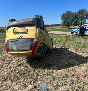 Leżący na dachu samochód, w tle stoi radiowóz