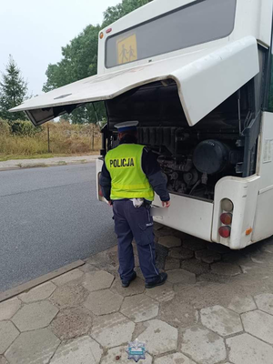 Policjant stojący za autokarem z uniesioną pokrywą silnika