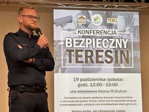 Policjant z mikrofonem, a w tle plakat informujący o konferencji