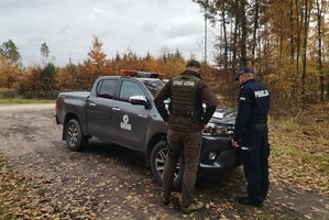 Policjant i strażnik leśny stoją przy pojeździe służbowym.