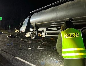 Samochód ciężarowy sto na skraju jezdni. Przed samochodem stoi policjant w odblaskowej kamizelce i strażacy