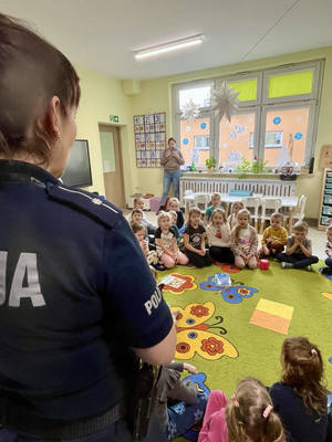 Dzieci siedzące w klasie na dywanie i policjantka