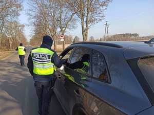 Policjanci stoją na drodze. Jeden z nich bada trzeźwość kierowcy