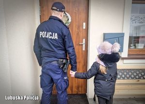 Policjant stoi przed drzwiami wejściowymi.  Za rękę trzyma dziewczynkę