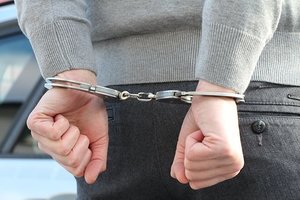 obraz przedstawia mężczyznę z założonymi kajdankami na ręce trzymane z tyłu