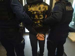 Policjanci trzymają pod ręce skute kajdankami mężczyznę w bluzie