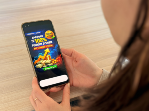 Telefon trzymany w dłoniach kobiety. Na wyświetlaczu wyświetla się reklama zachęcająca do inwestowania