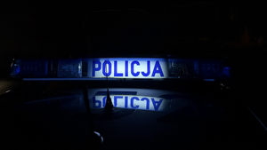 Zdjęcie robione nocą. Na dachu radiowozu świeci napis policja